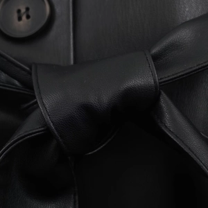 Dettaglio cappotto nero in finta pelle con grande bottone e cintura annodata in vita