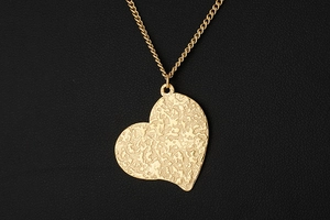 Close-up of gold heart pendant necklace with unique irregular texture on black background