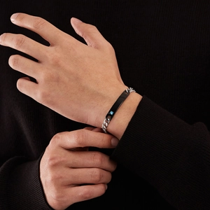 Polished silver Cuban link bracelet with black rectangular plate worn over a black sweater