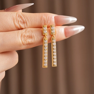 Détail de boucles d'oreilles pompons carrées en zircone cubique au fini doré chic