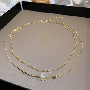 Detail of double-layer gold chain necklace featuring an iridescent pearl and snake chain