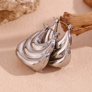 Macro shot of silver-toned hollow boat earrings with layered wave textures on wood