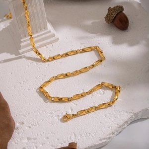 Minimalist gold geometric chain necklace displayed on a textured surface with decor