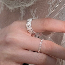 Macro shot of silver woven texture and wavy band ring set worn on finger in soft light