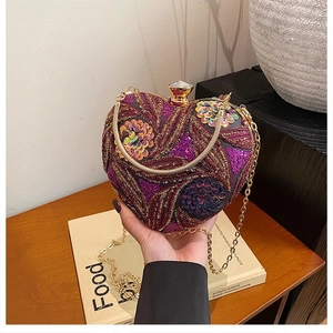 Detail of heart-shaped sequin clutch with embroidery and golden chain held by hand