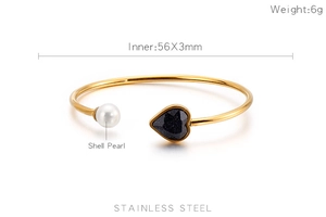Macro shot of gold stainless steel open bangle with heart stone and shell pearl detail