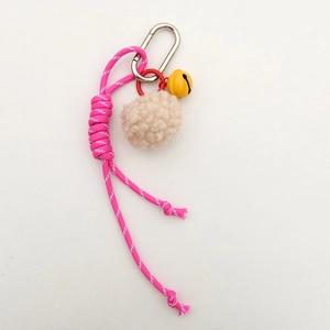 Pink braided nylon strap keychain with beige pompom and yellow bell detail