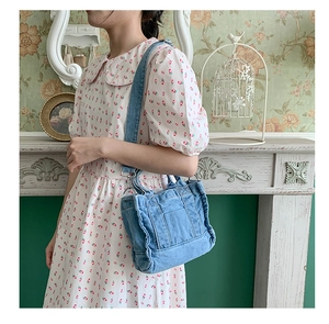 Detail of vintage blue denim crossbody bag with adjustable strap worn on a floral dress