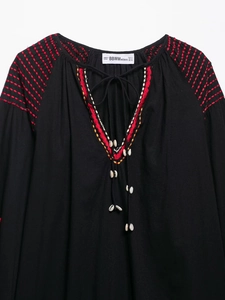 Détail de robe noire à col en V avec broderie rouge et ornements en coquillages blancs