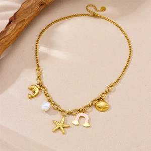 Detail of gold plated stainless steel necklace with ocean charms and pearl on sandy texture