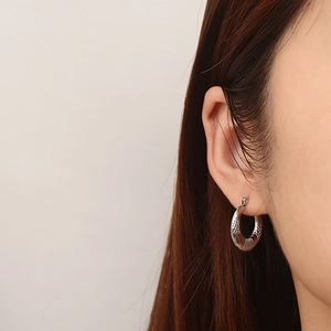 Close-up of a silver-toned U-shaped earring with snake skin texture on a model