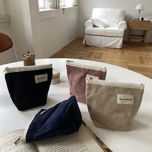 Four corduroy cosmetic bags in black, pink, beige, and blue on a table in a cozy room