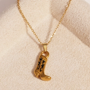 Vue détaillée d'un collier pendentif botte de cow-boy doré sur un tissu beige doux