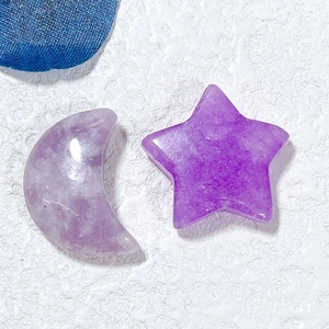 Macro detail of natural purple crystal moon and star carvings on a textured white surface