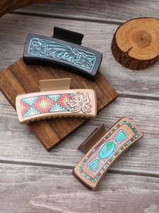 Three western cowboy style leather hair claws in navy blue, beige, and brown on wood base