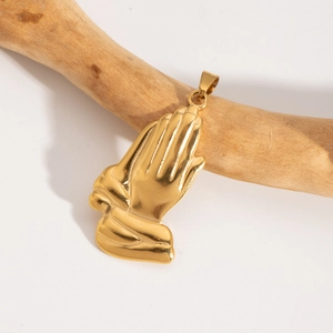 Détail d'un pendentif mains en prière doré suspendu à une branche de bois naturel