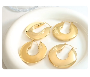 Macro shot of two pairs of thick gold C-shaped hoop earrings on a white display plate