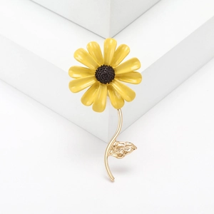 Elegant yellow daisy enamel brooch with golden metal leaves on a white background