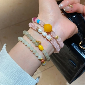 Détail de bracelets superposés en jade et ambre avec perles portés au poignet avec sac
