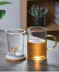 Detail view of transparent glass tea cup with yellow handle, glass filter and wooden base