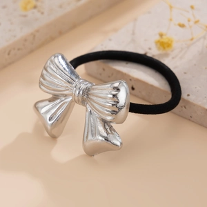 Close-up of a silver bow hair tie with textured finish on a beige stone surface