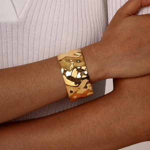 Close-up of a wide gold open cuff bracelet featuring a textured hammered finish on a model
