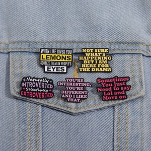 Detailed view of 5 unique enamel slogan pins on denim jacket showing diverse quote designs