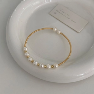 Close-up of golden spring cuff bracelet with natural freshwater pearls on ceramic dish