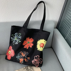 Detail of black canvas tote bag featuring six colorful artistic flower patterns on a sofa