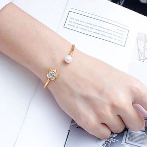 Gold-plated C-shaped open bracelet with crystal flower and pearl elements on woman's wrist