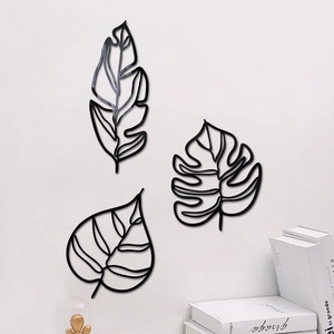 Détail de trois décorations murales feuilles en métal noir 3D sur un mur blanc minimaliste