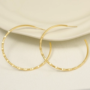 Exaggerated large matte gold hoop earrings with textured wavy surface on ceramic tray