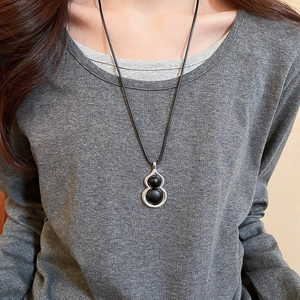 Détail du collier pendentif gourde minimaliste sur fond de pull en tricot gris