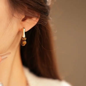 Detail of model wearing gold-plated beaded drop earrings with brown tiger eye beads