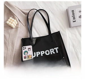 Detail view of a black semi-transparent PVC tote bag with white SUPPORT text on stylish bedding
