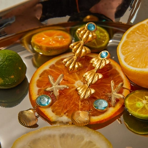 Golden shell and starfish earrings with blue gemstones displayed on citrus fruit slices