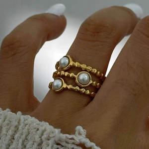 Detail of three stacked gold-tone rings featuring white pearls and textured bands on a finger