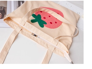 Close-up of the strawberry towel embroidery and zipper on a beige canvas tote bag