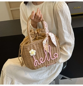 Detail of woven straw handbag featuring pink hello embroidery and floral scarf accent