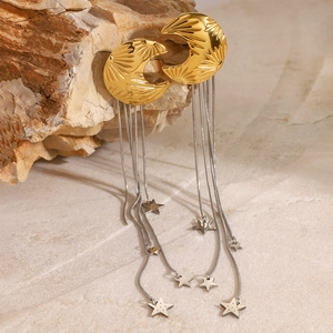 Detail of gold crescent moon earrings with silver tassels and star charms on a stone