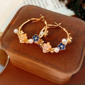 Macro shot of vintage gold hoops with enamel flowers and white pearls on velvet