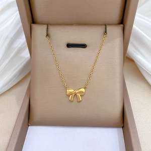 Macro detail of gold-plated titanium steel bow necklace on elegant silk jewelry box
