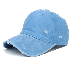 Detailed view of frayed holes and worn edges on a washed light blue denim baseball cap