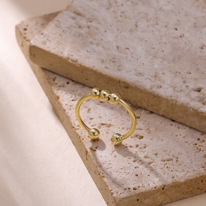 Macro view of adjustable gold snake ring with sliding beads on a travertine stone background
