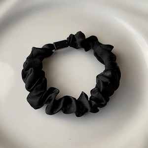 Detail of black satin scrunchie with rectangular buckle on white ceramic tray