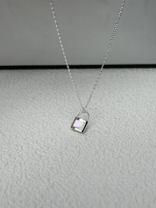 Close-up of silver padlock pendant with white mother of pearl inlay on a minimalist chain