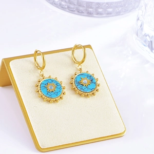 Detail of gold sunburst hoop earrings featuring turquoise stones on a beige stand