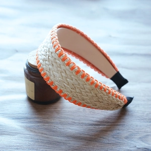 Detail of beige raffia woven headband with orange stitching on a rustic wooden background