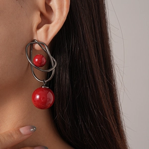 Detail view of red acrylic balls on geometric dark grey metal wire earrings worn by model