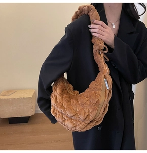 Detail of a brown quilted crescent bag featuring velvet texture and pleated shoulder strap